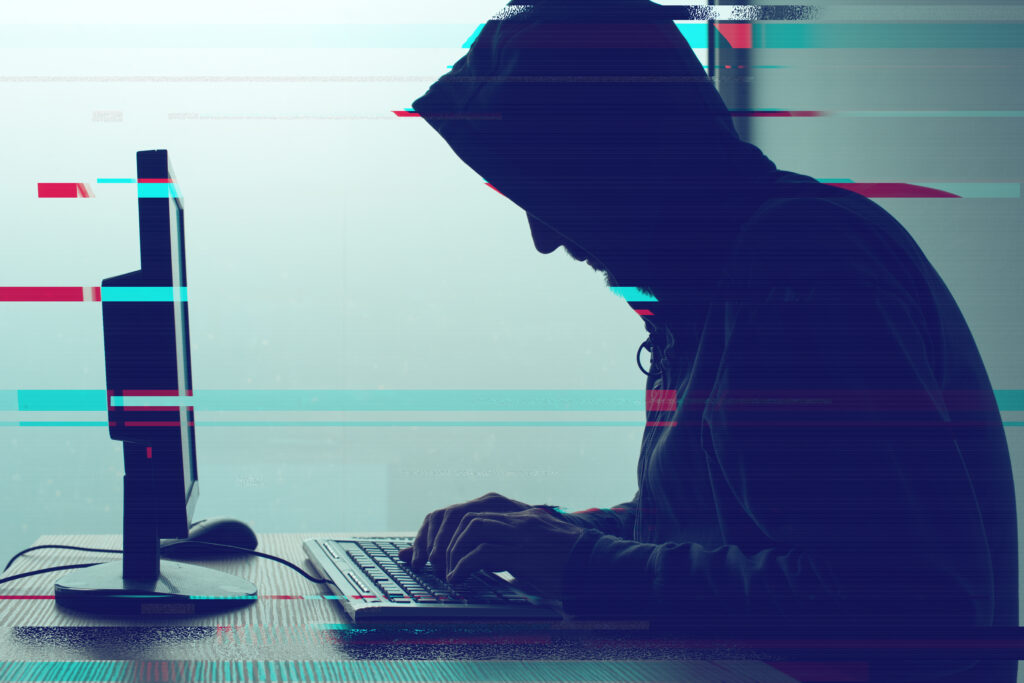 Hooded computer hacker working on desktop PC computer